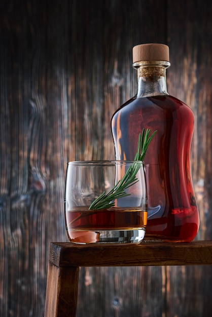 A round glass with a shot of whiskey and a sprig of rosemary