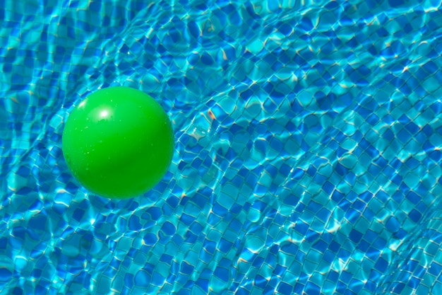 Round green ball on the surface of the water in a pool with blue water and waves The concept of children's safety near the water