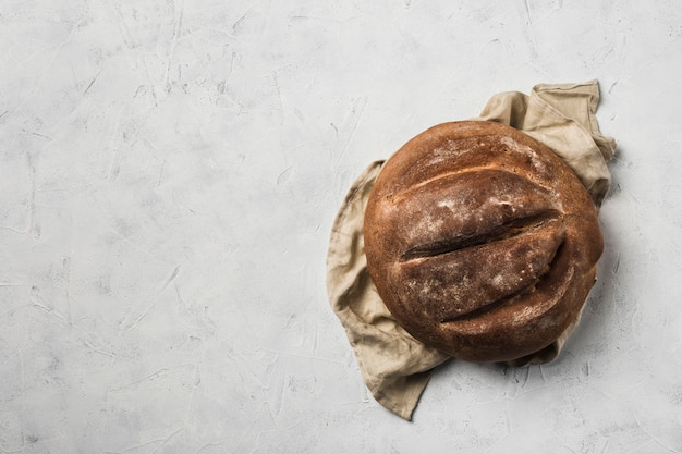 A round loaf of bread lies on a grey linen napkin against a light background. top view with copyspace.