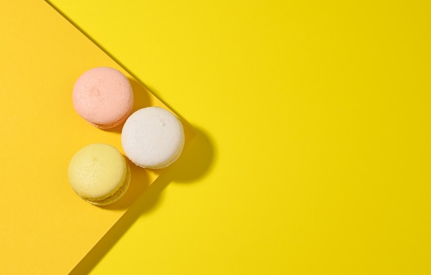 Round multicolored macarons on a yellow surface with a shadow on a yellow surface. Gourmet almond flour dessert, top view