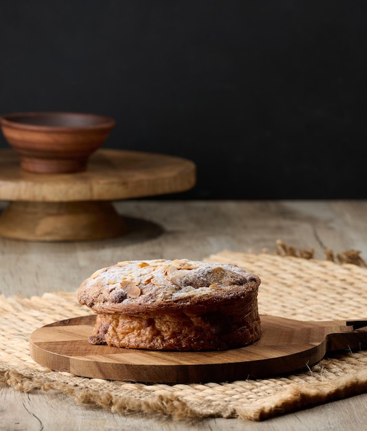 Round pastry with almonds and butter sprinkled with powdered sugar on the table puff pastry