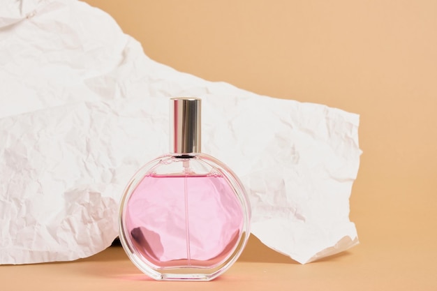 Round perfume bottle with a silver cap on a background of white crumpled paper, pink perfume