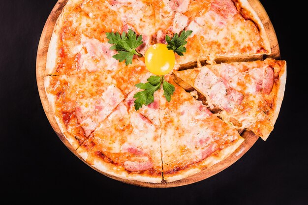 Round pizza with an egg on a wooden board on a black background