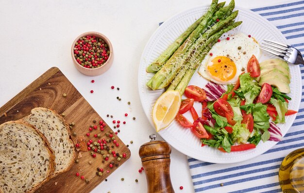 Round plate with cooked asparagus fried egg avocado and fresh vegetable salad on the table top view