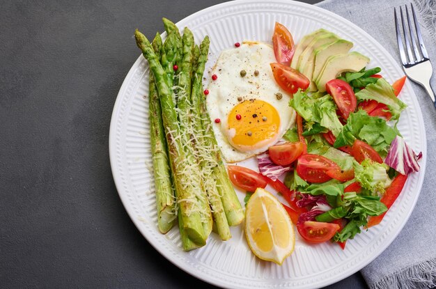 Round plate with cooked asparagus fried egg avocado and fresh vegetable salad on the table