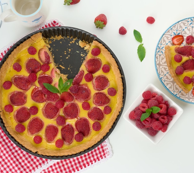 Round quiche with red strawberries and raspberries on a white table top view