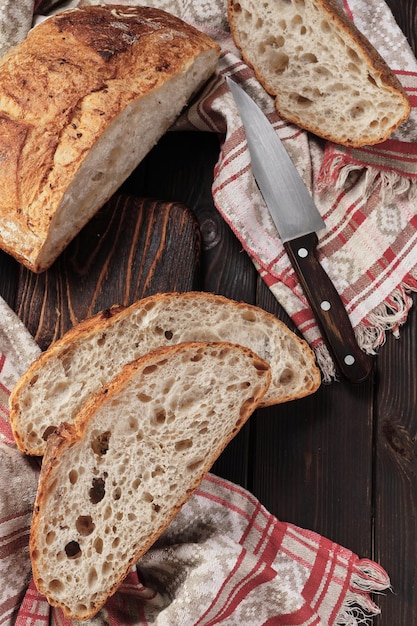 Round rustic bread without kneading cut into pieces on a cutting board on an old dark rustic table Homemade whole grain bread layout on the table vertical frame