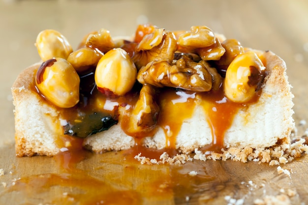 Round-shaped tartlet with nuts and dried fruits poured with caramel, the ingredients used in the tartlet are hazelnuts, peanuts, dried apricots, dried plums, walnuts