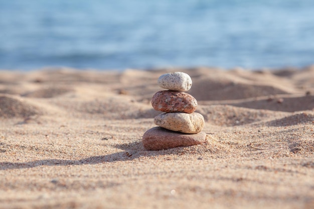 Round stones lie on top of each other in a column on the seashore on a sunny summer day.