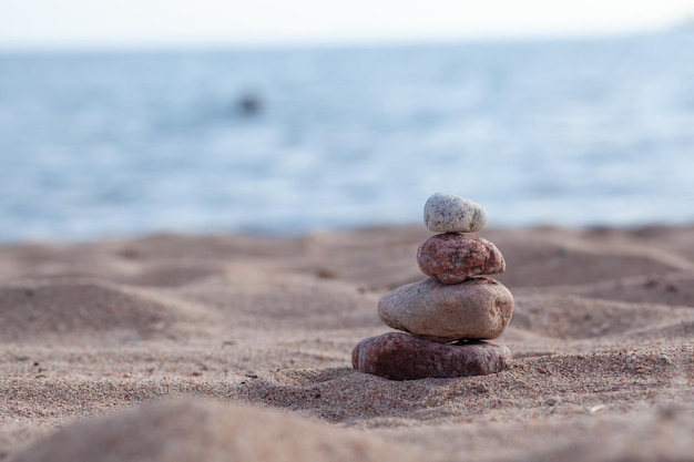 Round stones lie on top of each other in a column on the seashore on a sunny summer day.