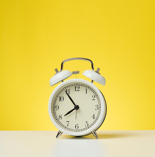 Round white alarm clock, five minutes to eight in the morning. Yellow background