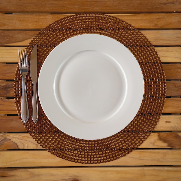 Round white plate and embase wooden cutlery. Top view.