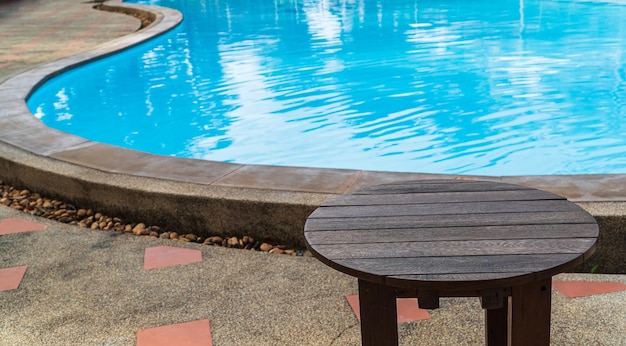 Round wood table foreground with empty swimming pool well editing products present on floor