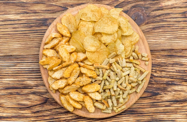 Round wooden board with dry salty snacks for beer on the table Top view