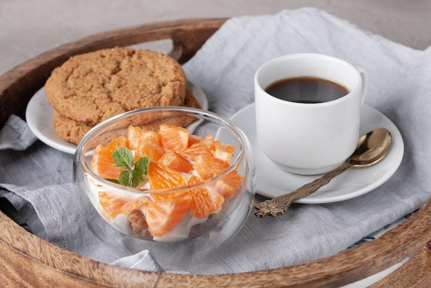 Round wooden tray with tangerine yogurt oatmeal cookies a cup of black coffee