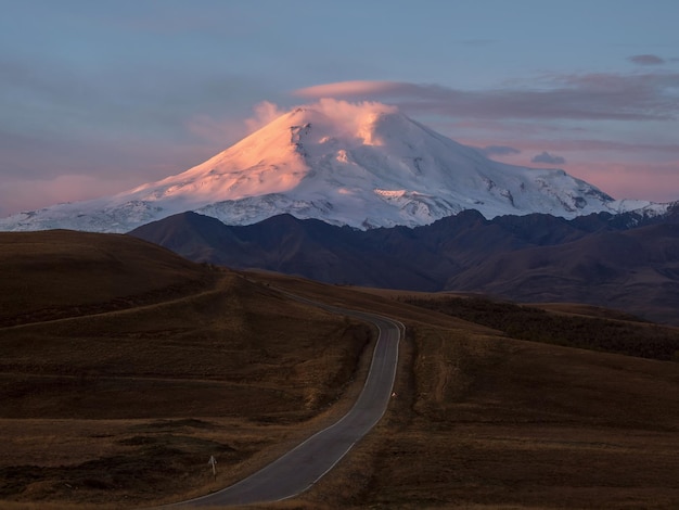 The route to the dawn Elbrus Pink majestic dawn over Mount Elbrus Snowy mountain peaks at dawn Sunset in magenta tones Atmospheric purple landscape with a highaltitude snowy mountain valley