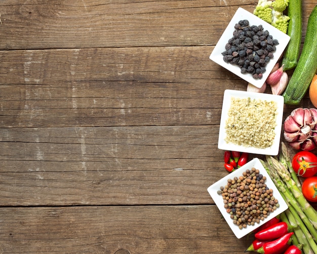 Roveja, hemp seeds and black chickpea in bowls and vegetables on a wooden table top view with copy space