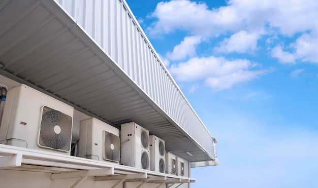 Row of air conditioner compressors on white wall under steel roof eaves of modern convenience store