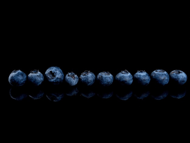 Row of blueberries on a black glossy background