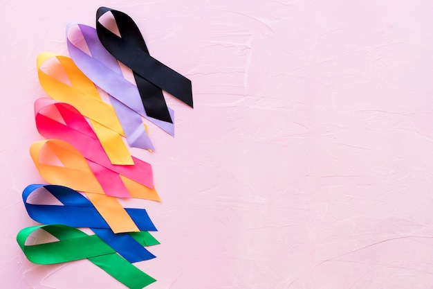 Row of bright colorful awareness ribbon on pink rough background