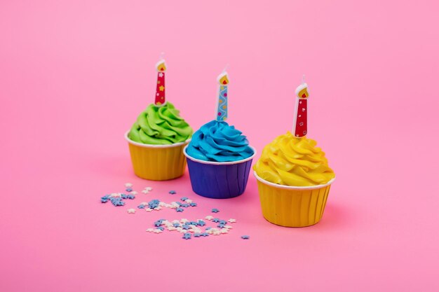 A row of colorful cupcakes with candles on a pink background