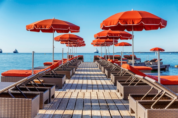 A row of deck chairs with orange mattresses and umbrellas in a fashionable resort. 