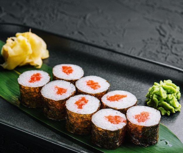 Row of fresh maki sushi rolls on black plate