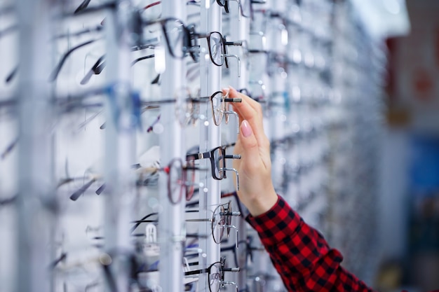 Row of glasses at an opticians. Eyeglasses shop. Stand with glasses in the store of optics. Woman's hand shows glasses. Presenting spectacles. Closeup