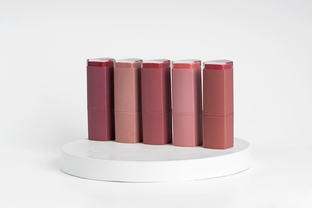 A row of lipsticks of different colors standing on white podiums demonstration production line