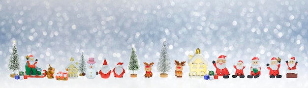 Row of little Santa Claus dolls and Christmas decorations on snowing background in panoramic view