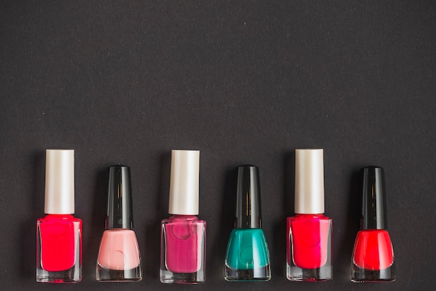 Row of multi colored nail varnish bottles on black background