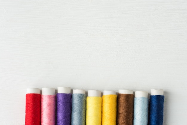 Row of multicolored sewing threads on cardboard spools. White wood background.