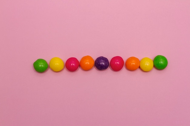 A row of rainbow coloured sweets on pink background