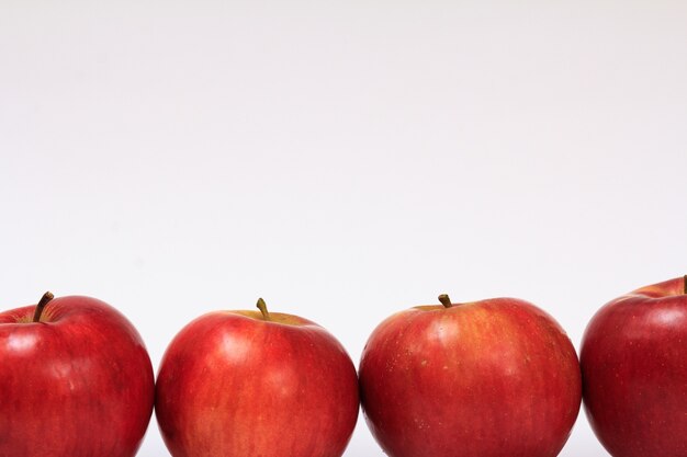 Row of ripe red apples on a white background with shadow.