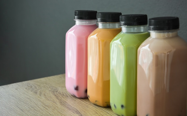 A row of various bobble tea in plastic bottles on wooden table with black color background