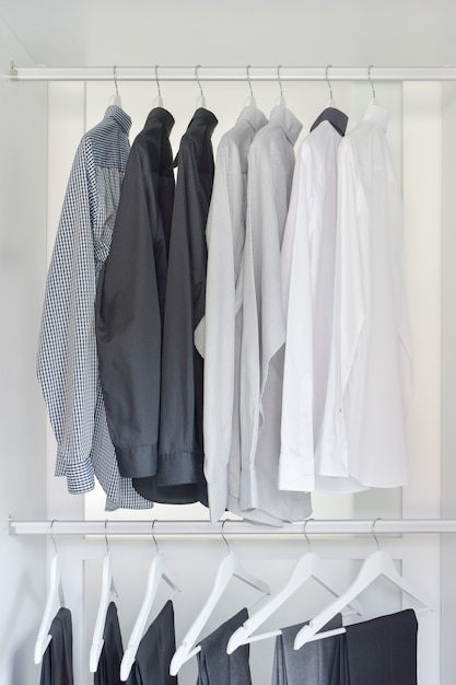 Row of white, gray, black shirts with pants hanging in wooden wardrobe