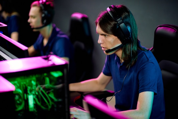 Row of young contemporary operators with headsets sitting in armchairs in front of computer monitors in call center and consulting clients