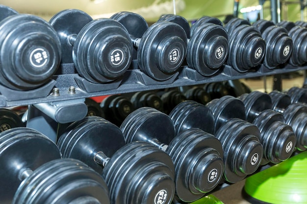 Rows of black dumbbells of different weights in the gym Sport activity and health Closeup