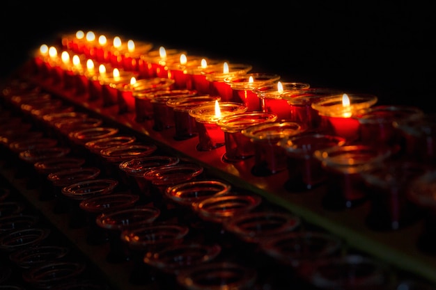 Rows of burning candles in the dark. Prayers and memory. Close-up. Space for text.