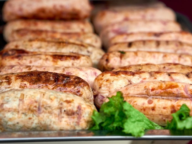 Rows of freshly grilled chicken meat sausages on tray with fresh lettuce