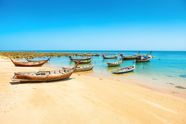 Rows of many traditional wooden fishing long tail boats moored at tropical sand beach with rocks