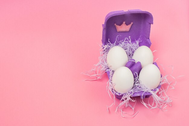 Royal easter eggs in purple carton box for eggs on pink background. Place for text