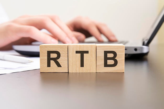 Rtb acronym from wooden blocks with letters background hands on a laptop with blur business concept