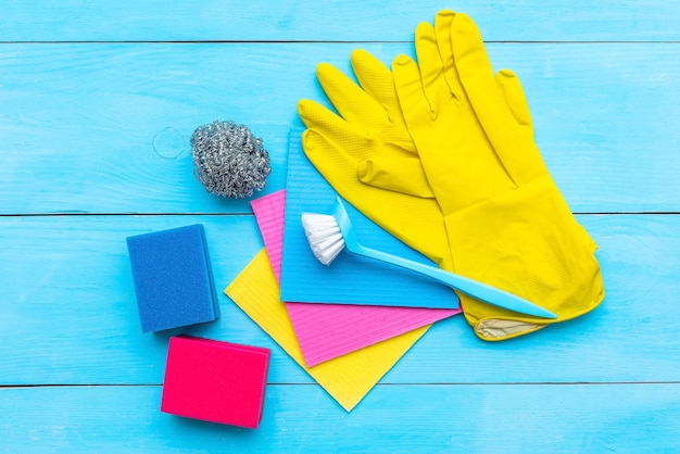 Rubber gloves, brush and cleaning cloths on blue, flat lay