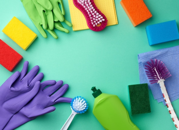 Rubber gloves for cleaning, multi-colored sponges, brushes and cleaning fluid in a green plastic bottle on a green surface