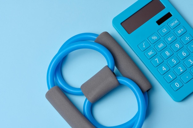 Rubber sports simulator expander and a calculator on a blue background top view calorie counting