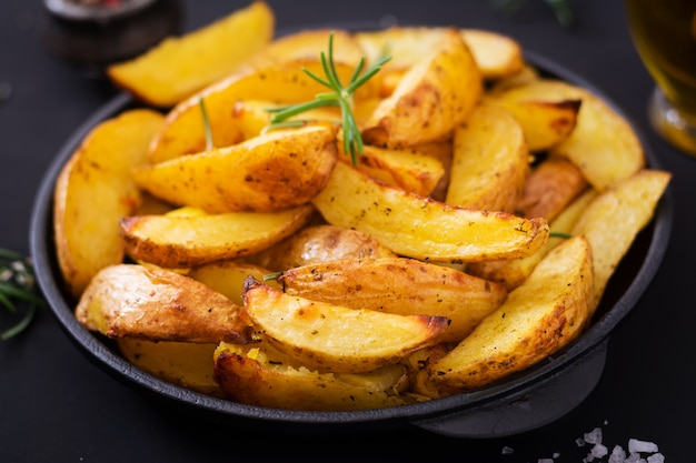 Ruddy Baked potato wedges with rosemary and garlic on a dark background.