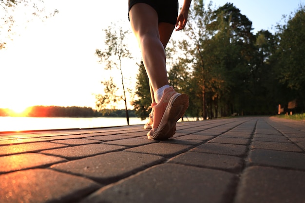 Runner feet running on road closeup on shoe, outdoor at sunset or sunrise.