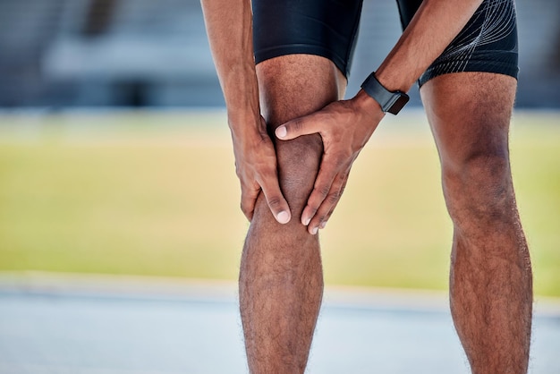 Runner knee injury and pain in legs on field track or sports at training workout or exercise Black man sport and knee pain emergency in running for health wellness or muscle development outdoor