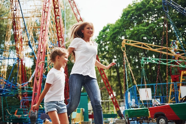 Running and playing. Cheerful little girl her mother have a good time in the park together near attractions.